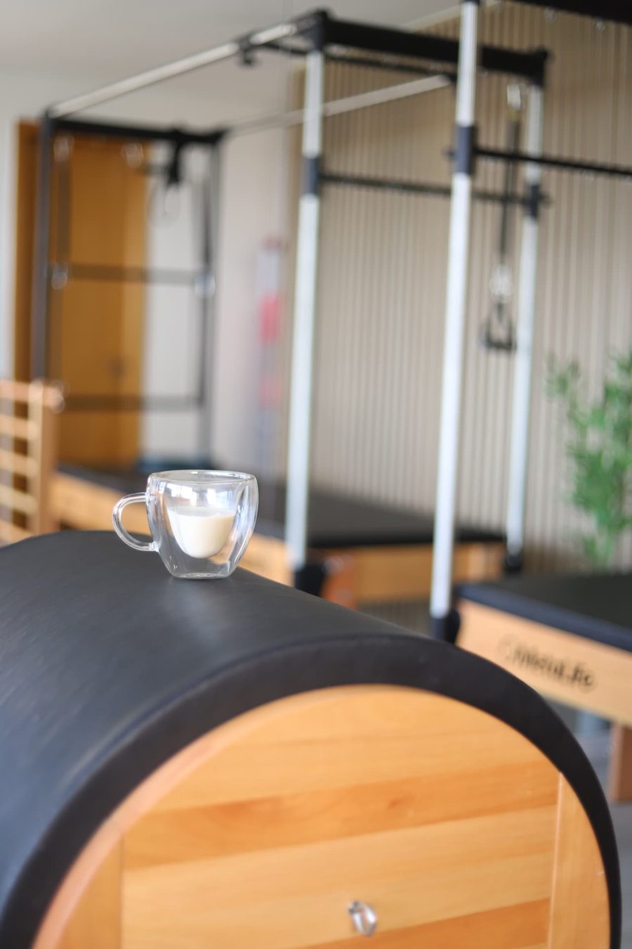 Detalhe do cuidado no estúdio Sublime Pilates: xícara de café apoiada em um barrel, com o estúdio ao fundo